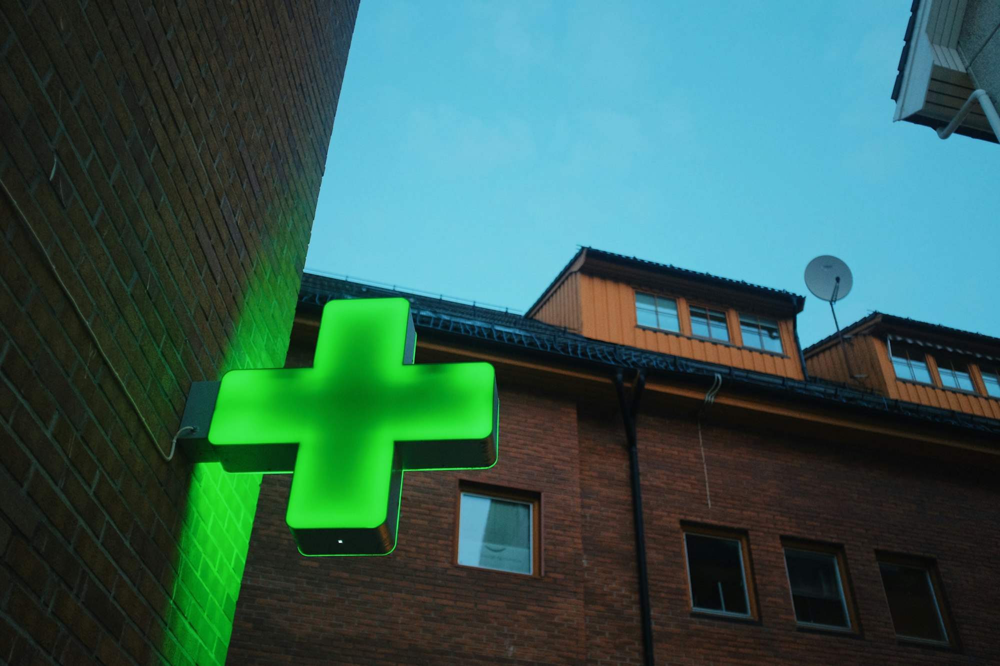 green neon cross, pharmacy/hospital sign on a building, evening blue light
