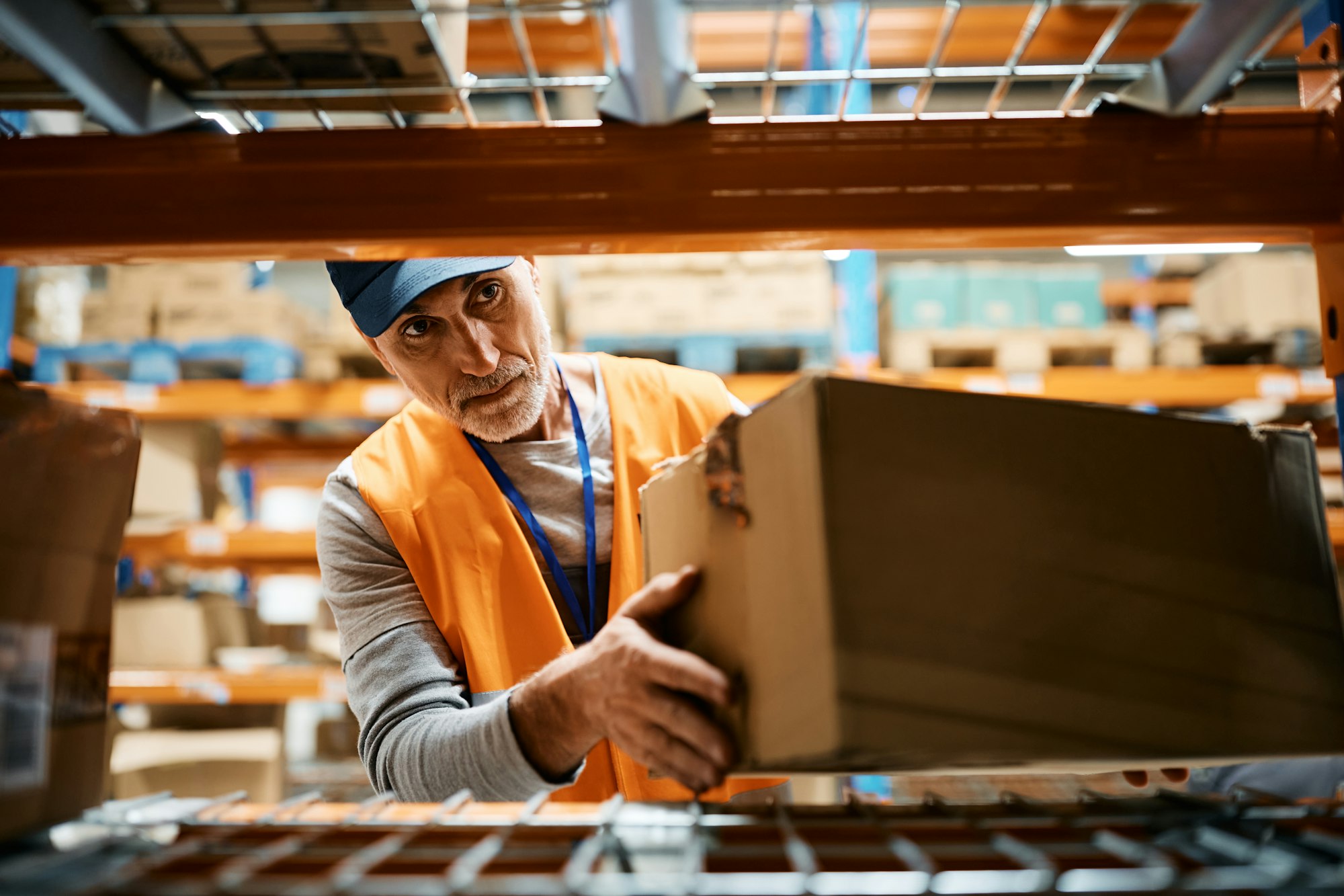 Mature worker stacking packages on racks while working at distribution warehouse.
